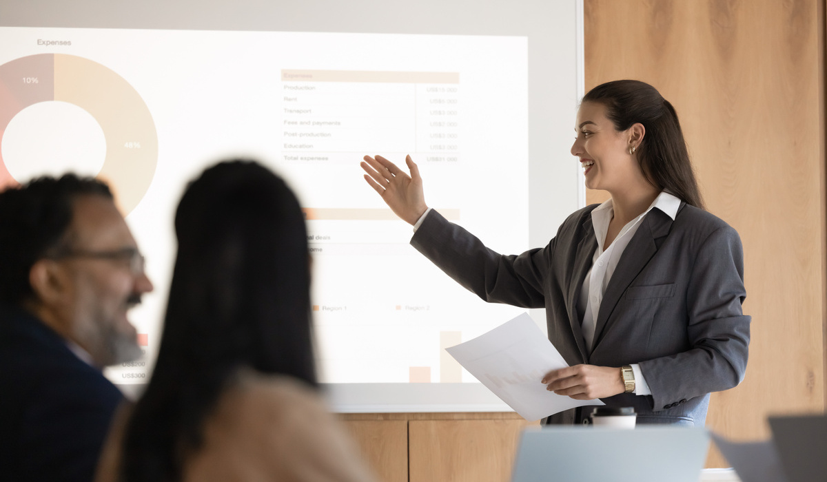 Business presentation and public speaking. Confident young businesswoman project manager executive speak at boardroom to diverse audience present statistical financial report using digital whiteboard